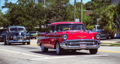 Classic cars lined up in a parade on a residential street for Burning Up the Beach